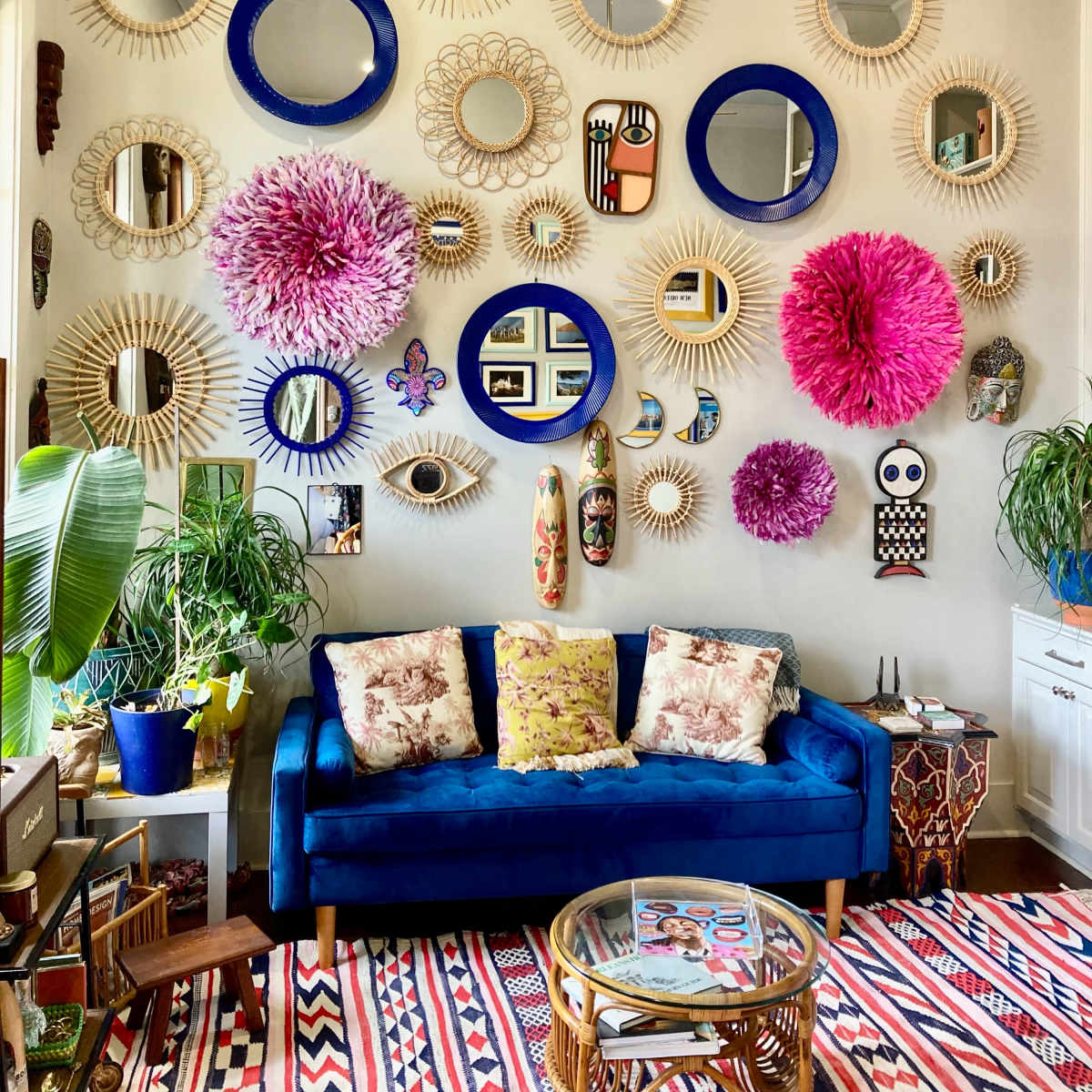 A vibrant living room wall adorned with various decorative mirrors and wall art, complemented by a blue couch and a patterned rug.