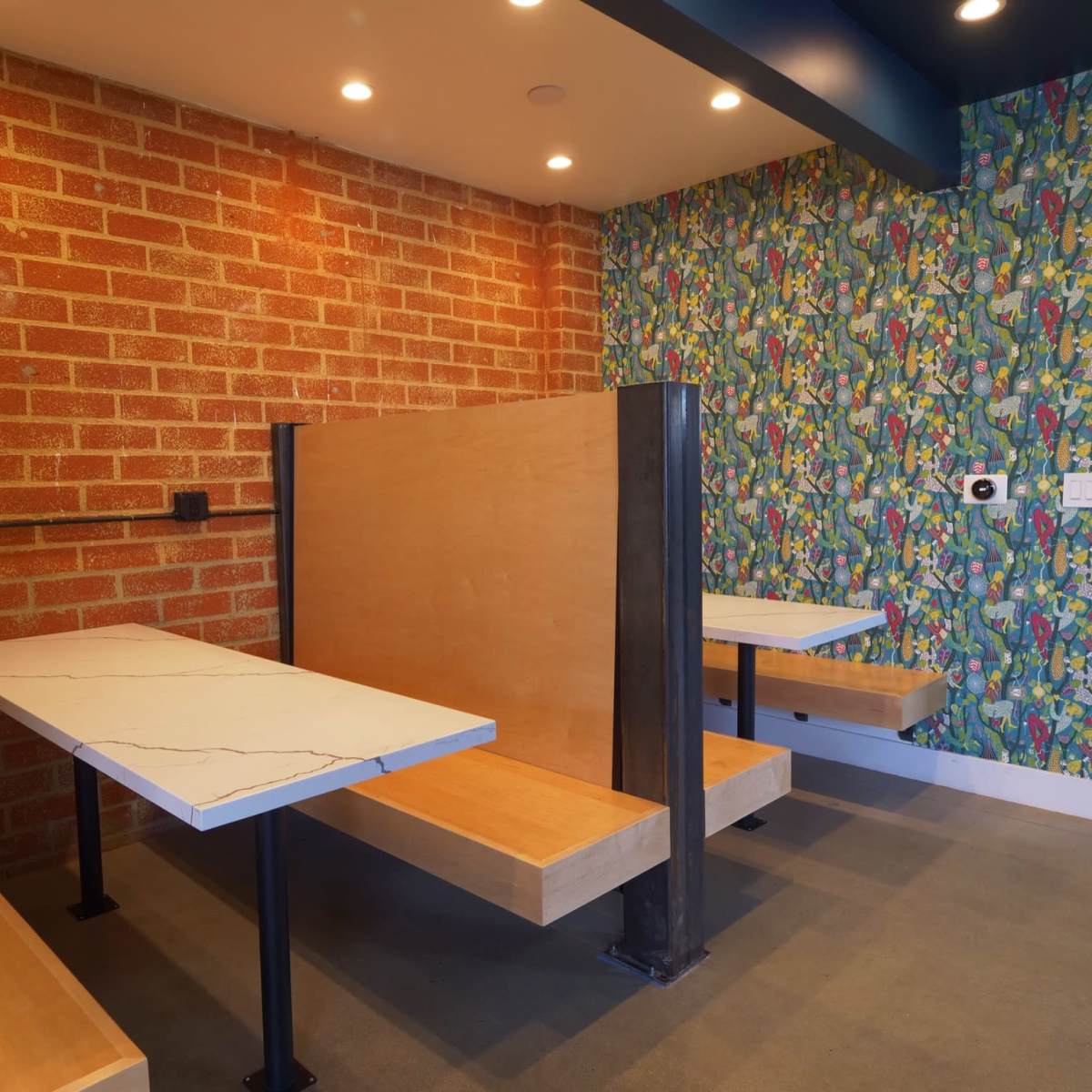 A modern seating area featuring two booth-style tables against a brick wall and a colorful patterned wall.