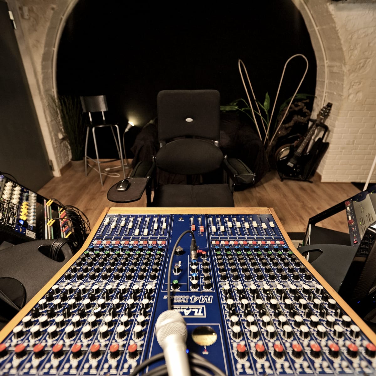 A sound mixing studio with a large mixing console at the center, flanked by two monitors, and a microphone positioned in front of a black chair.