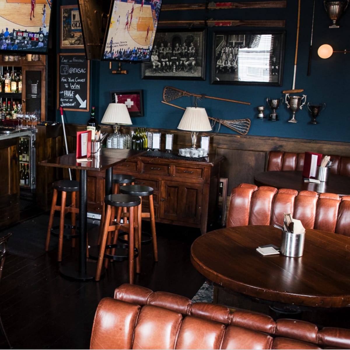 A cozy sports bar with wooden furniture, multiple television screens displaying basketball games, and a well-stocked bar in the background.