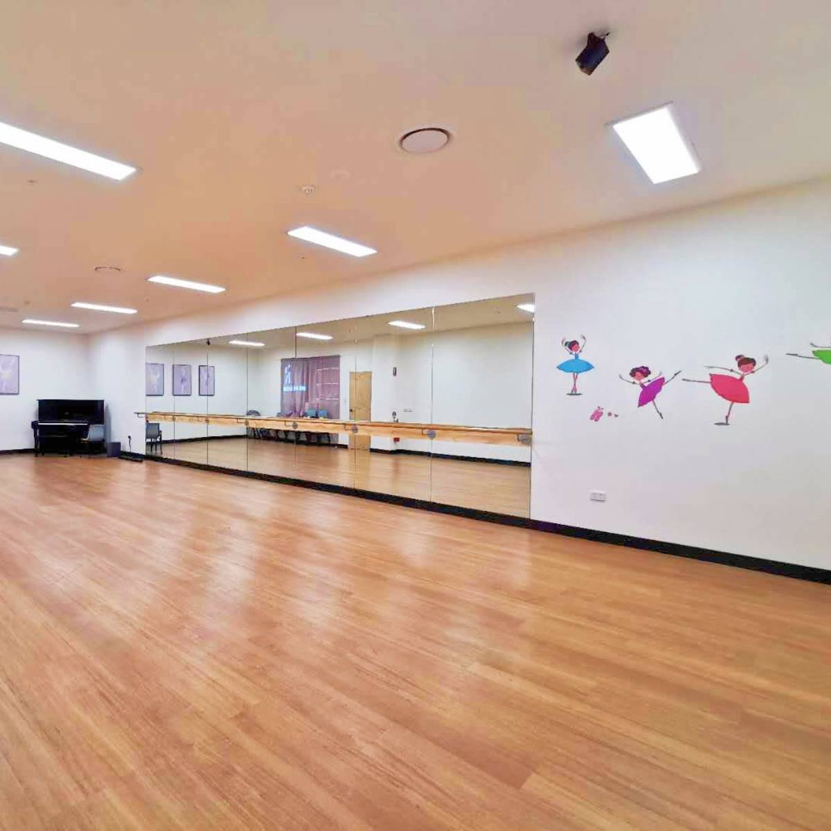 A spacious dance studio with wooden flooring, mirrors on one wall, and colorful ballet-themed decorations.