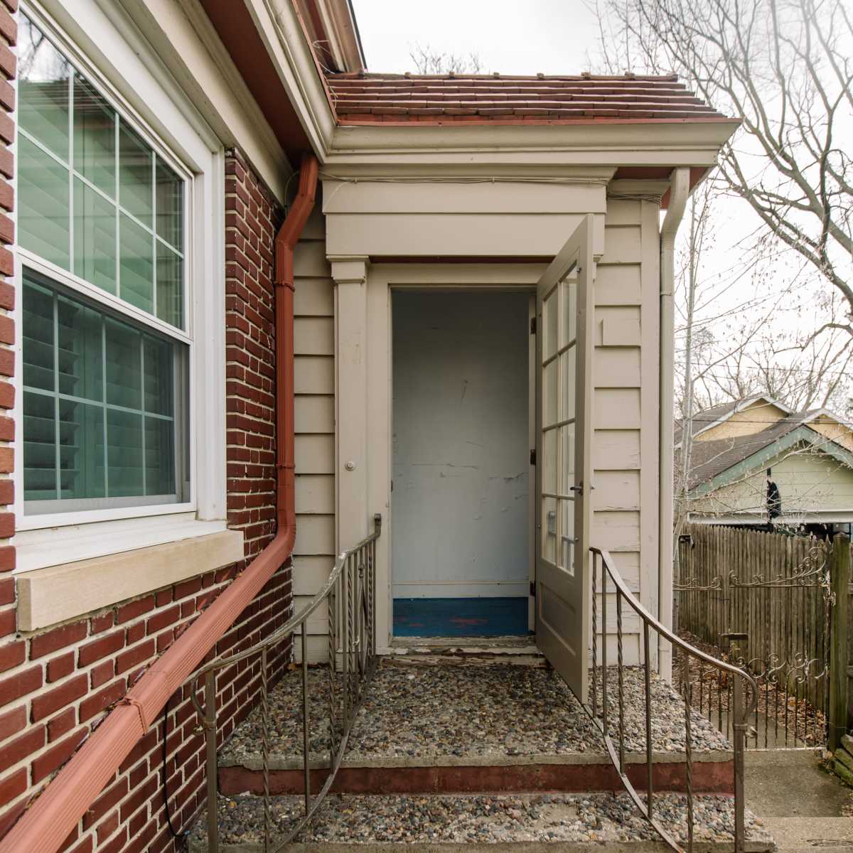 A front entrance with a staircase leading up to double doors in a brick and siding house, set against a cloudy sky.