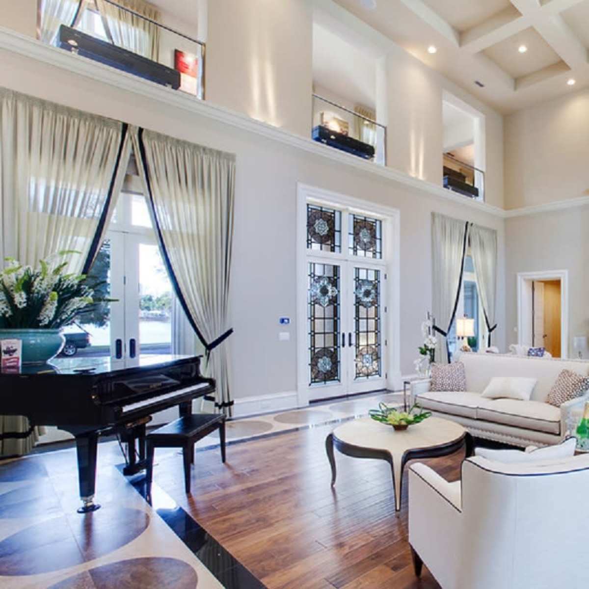A spacious living room with high ceilings, large windows, elegant furnishings, and a grand piano.
