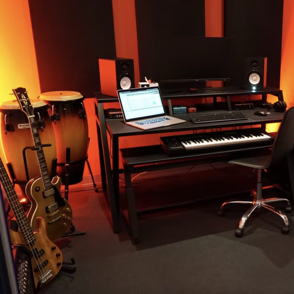 A music studio with a keyboard, computer, speakers, microphones, guitars, and soundproof panels on the walls.