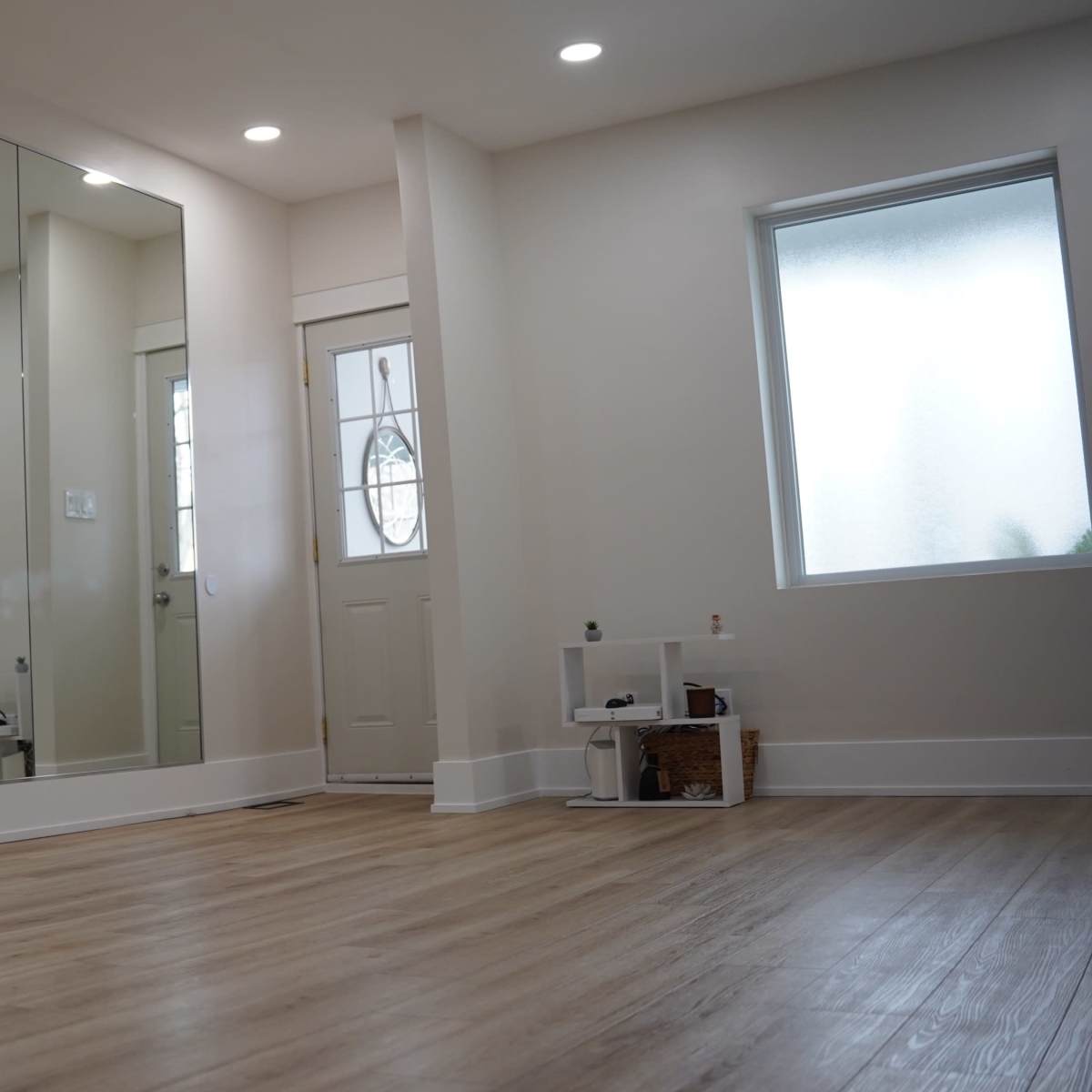 A spacious room with wooden flooring features a large mirror on one wall and a door leading outside.