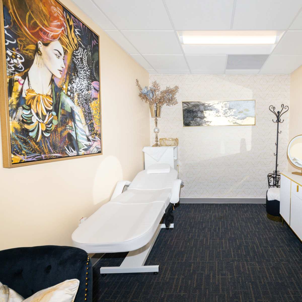 A serene treatment room featuring a massage table, a decorative mirror, and modern artwork on the walls.