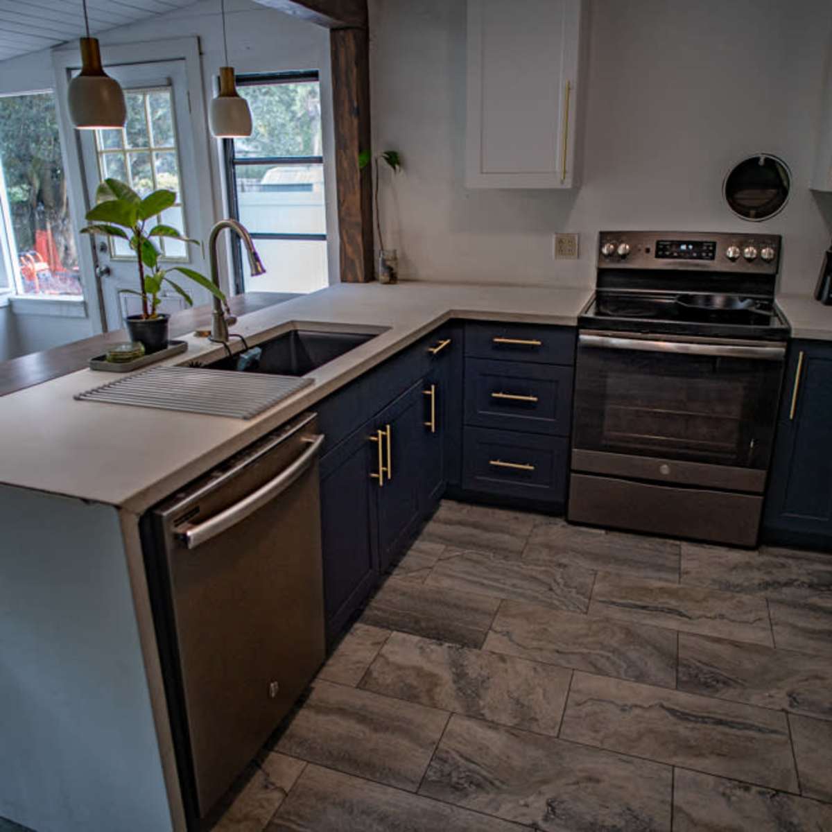 A kitchen features navy blue cabinets, a stainless steel oven, and a sink with a modern faucet, illuminated by pendant lights.