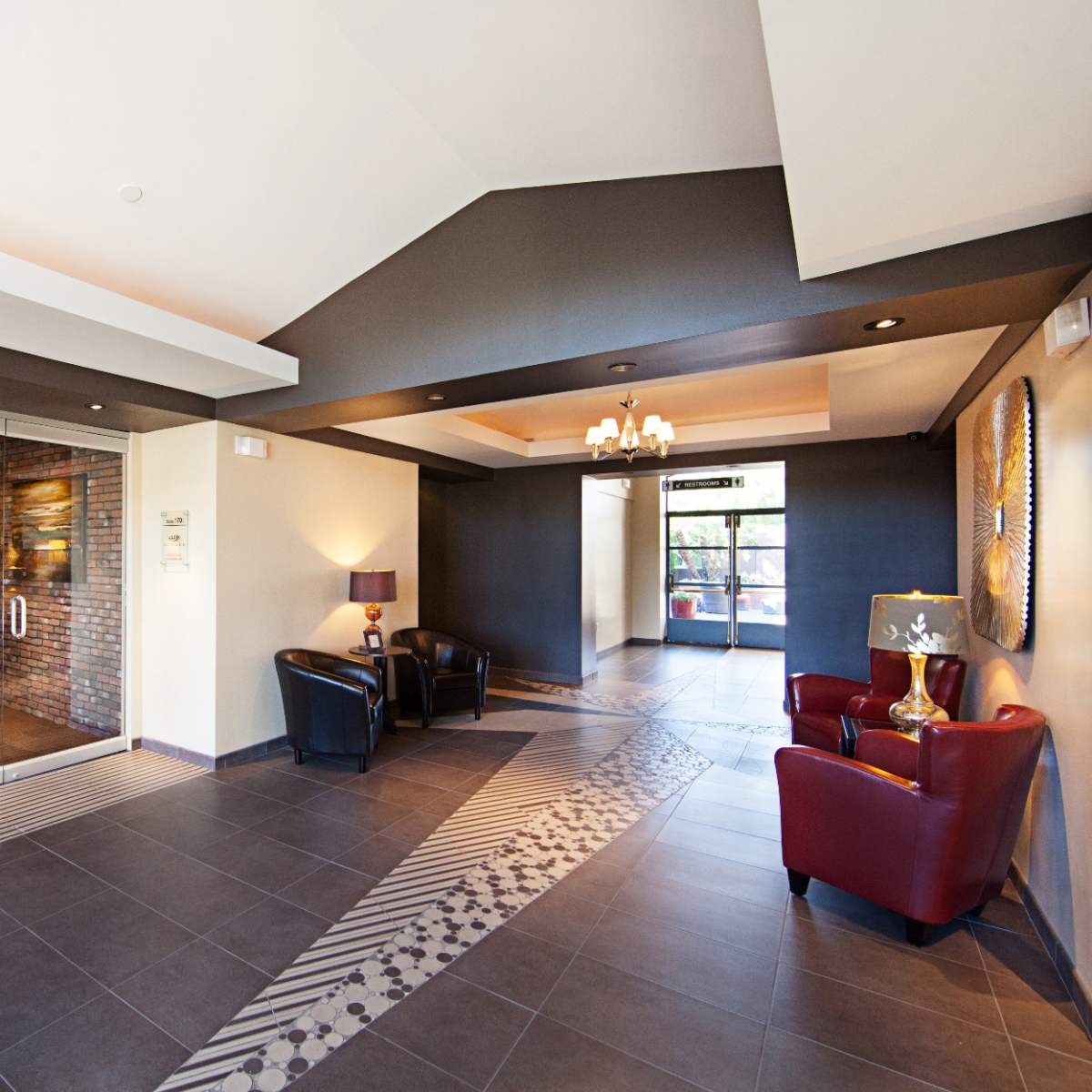 A modern lobby area featuring two leather chairs, a small table, and a reception area with glass doors leading outside.