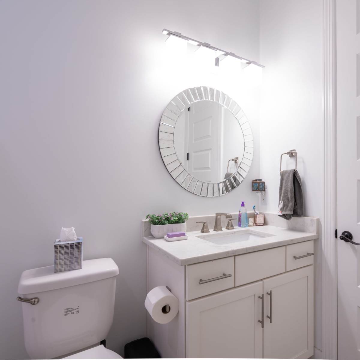 A modern bathroom featuring a white vanity with a circular mirror, a toilet, and a door, all set against a neutral wall.