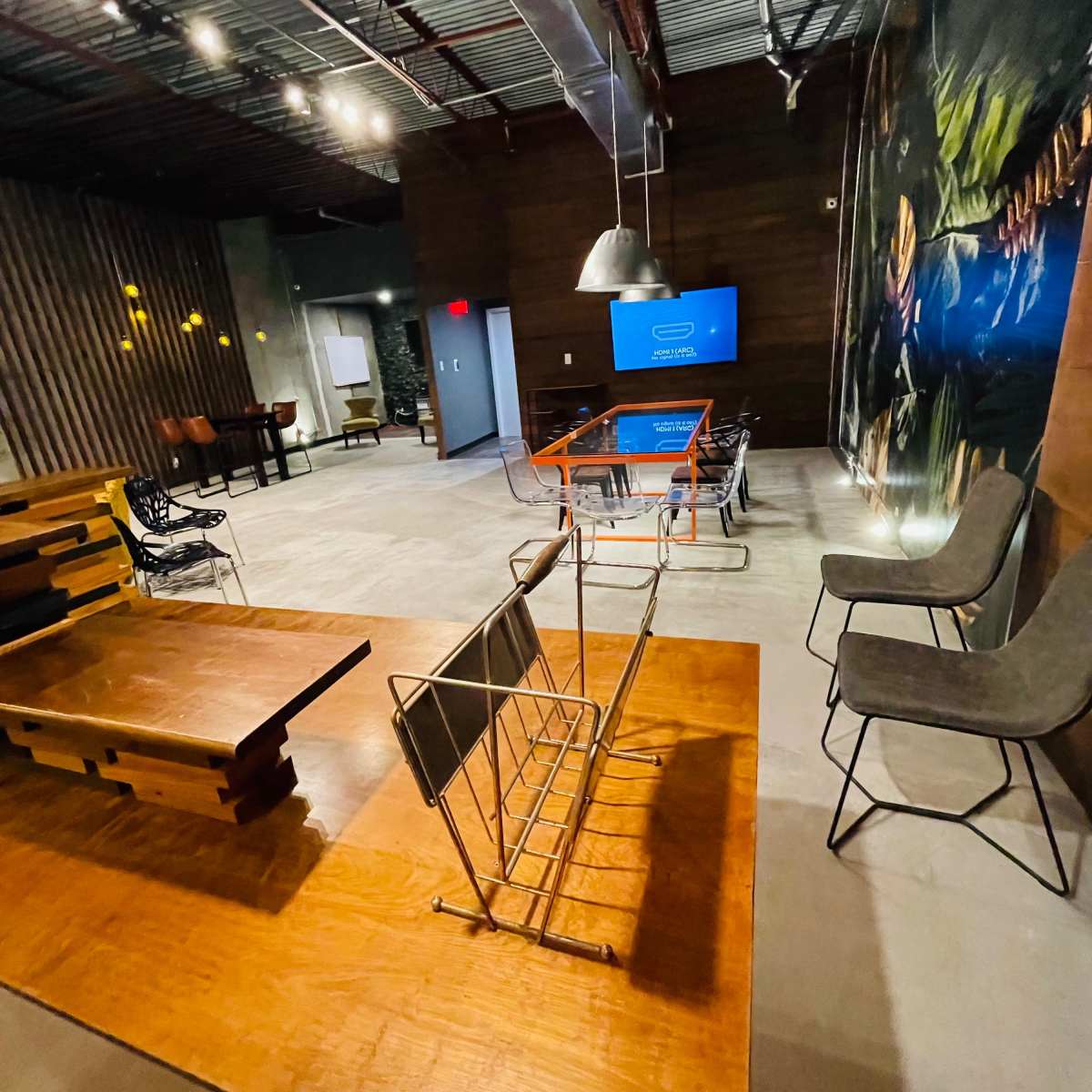 A modern meeting room with wooden furniture, stackable chairs, and a television mounted on the wall.