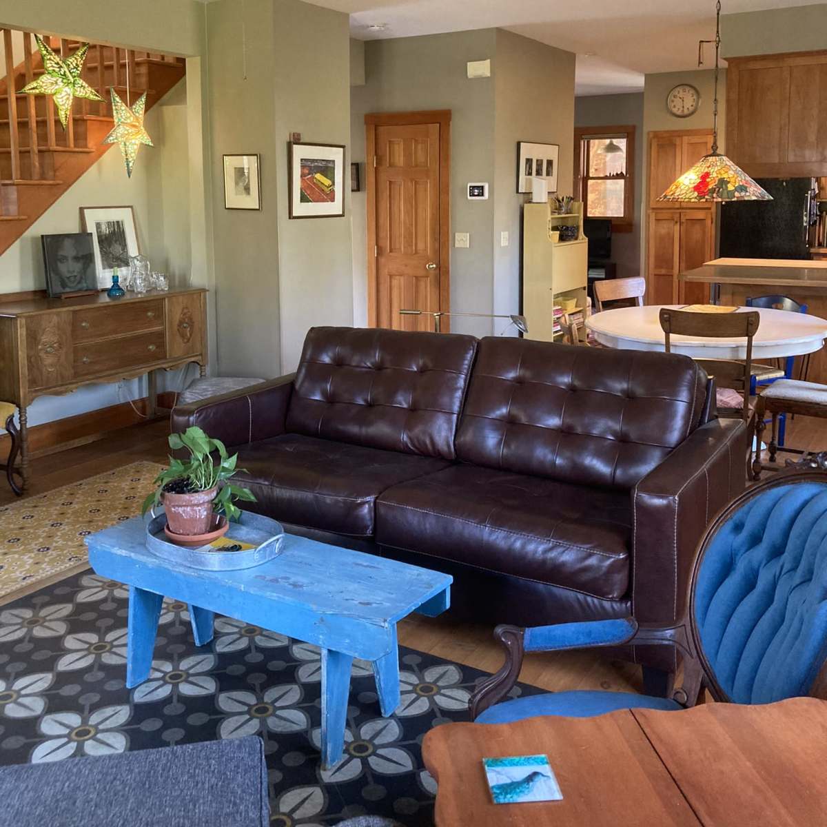 A living room with a brown leather sofa, a blue coffee table, and various light fixtures hanging from the ceiling, including star-shaped designs.