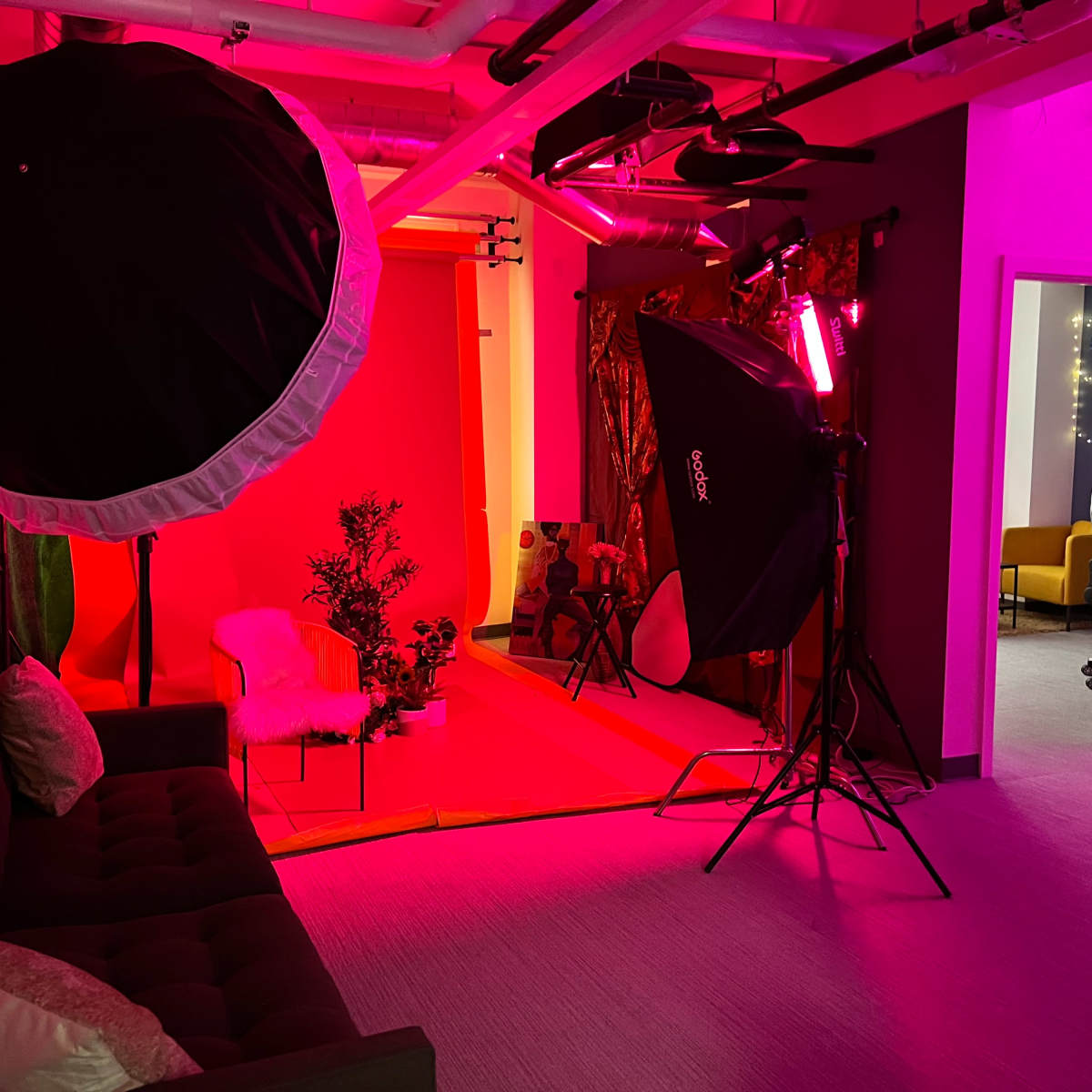 A photography studio with a red backdrop, lighting equipment, and a brown couch in a brightly colored space.