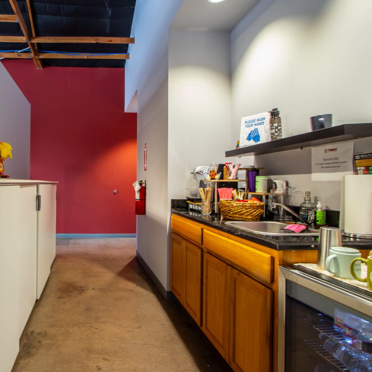 A narrow kitchen space with white cabinets on one side and wooden cabinetry on the other, leading to a brightly colored wall at the far end.