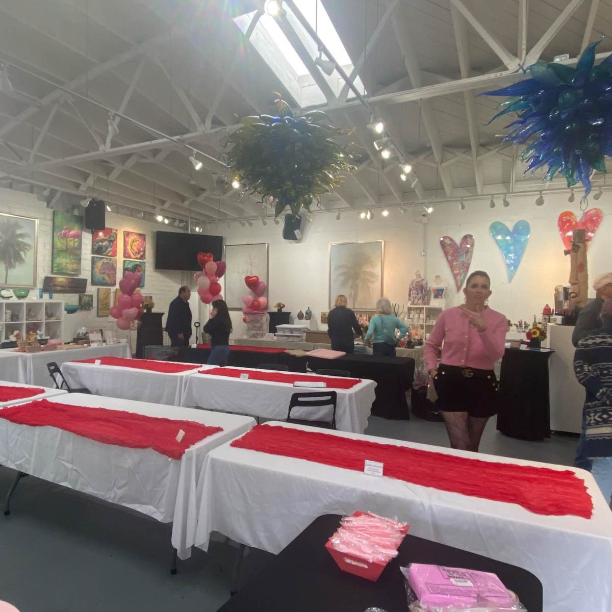The scene features an art gallery with tables covered in white tablecloths and red runners, decorated with balloons and artwork displayed on the walls.