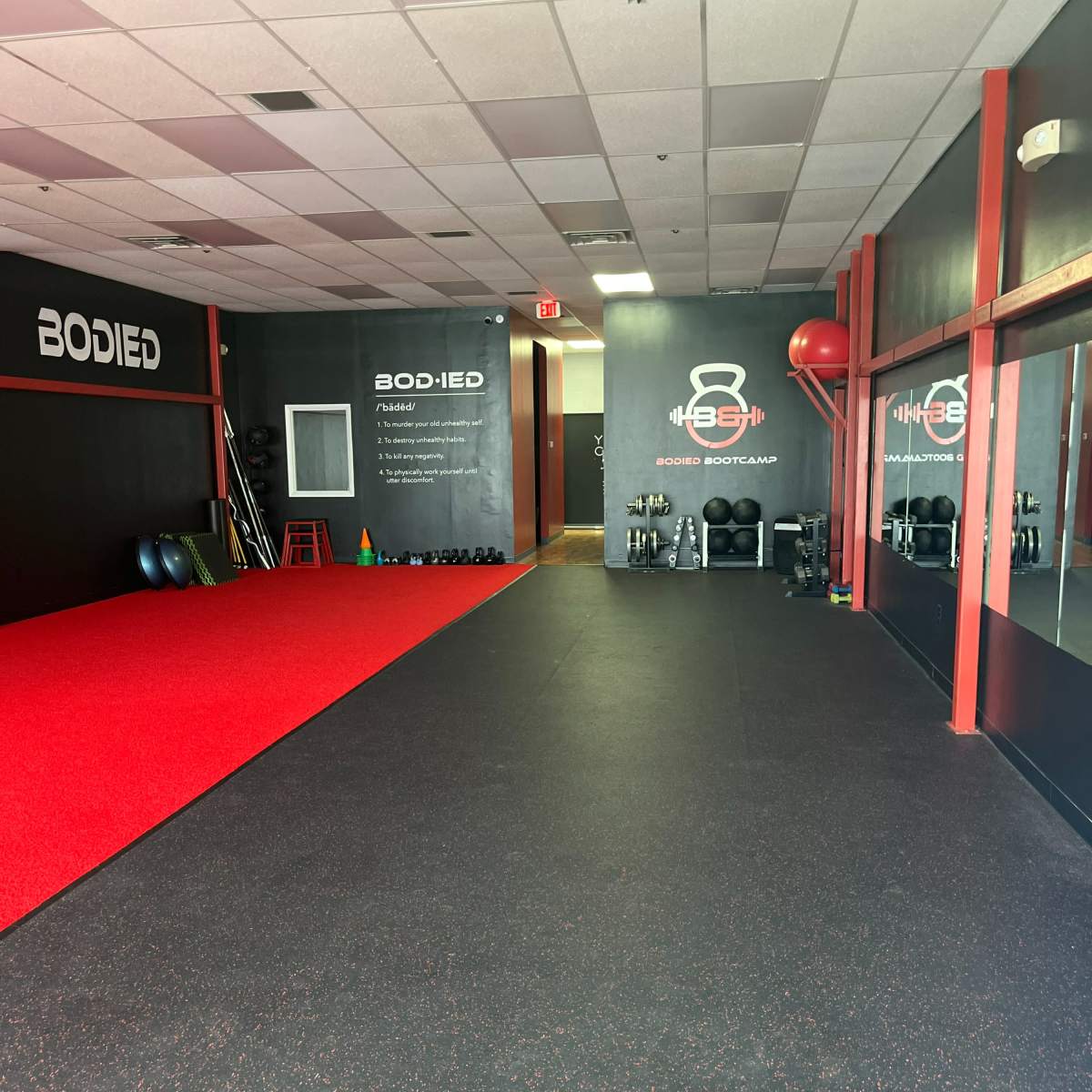 A fitness studio with rubber flooring, red accents, and exercise equipment along the walls.