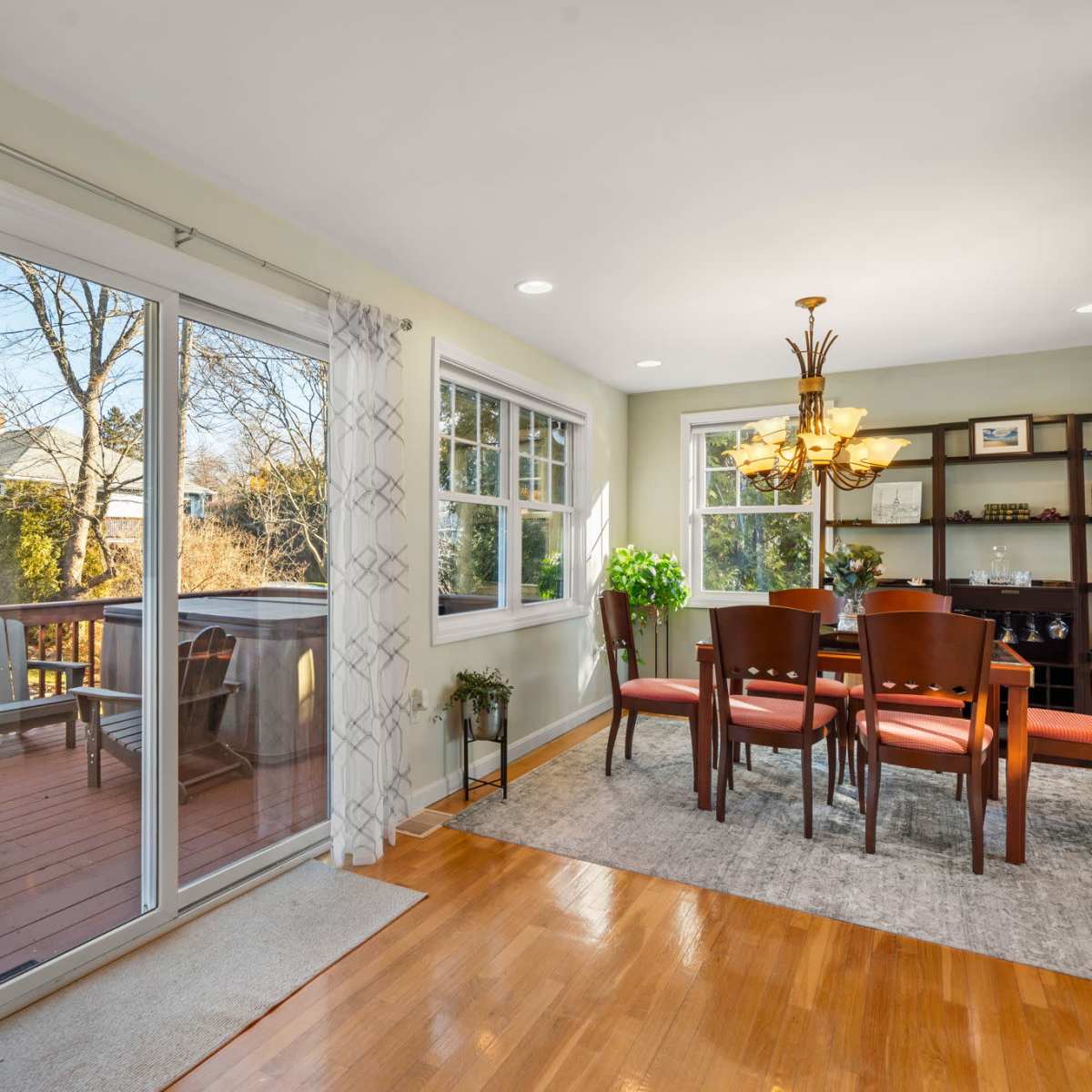 A bright dining area with a wooden table and chairs, adjacent to a glass door leading to an outdoor deck.
