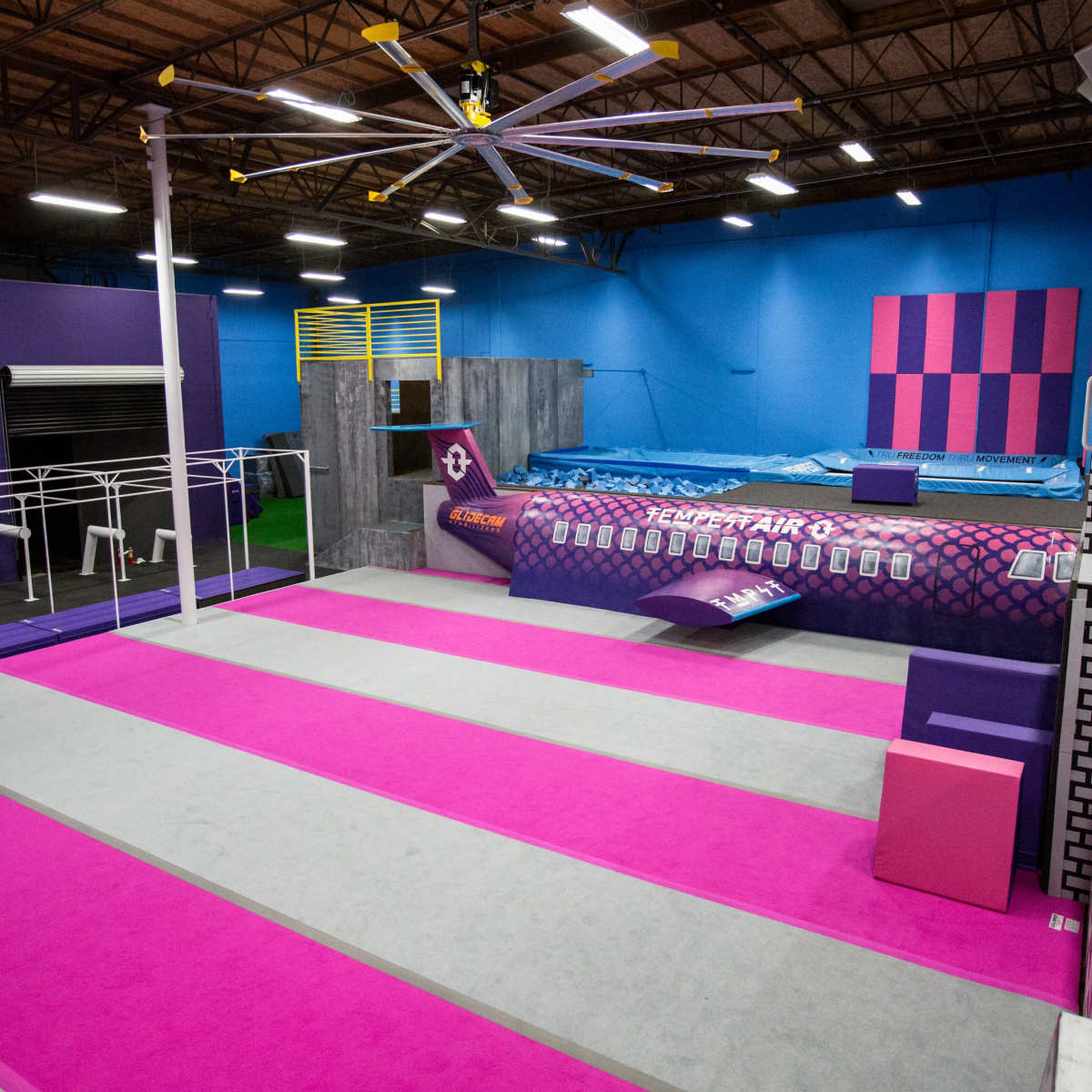 An indoor gym facility with colorful walls, various exercise equipment, and a large foam pit.