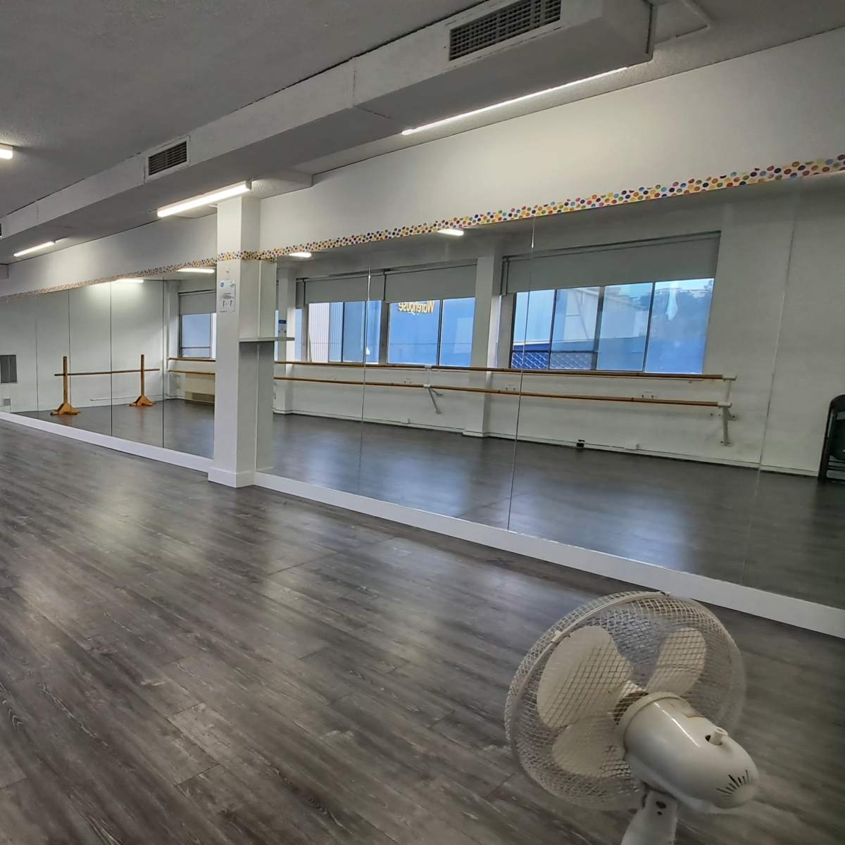 A spacious dance studio with mirrored walls, wooden flooring, and ballet barres along one side.