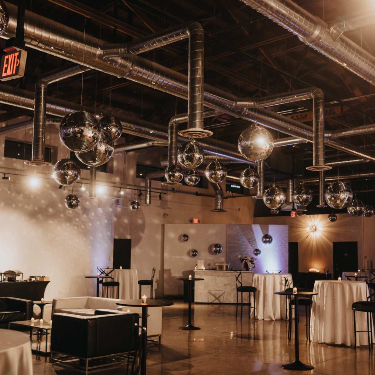 A spacious event venue with hanging disco balls and various tables set up, illuminated by soft lighting.