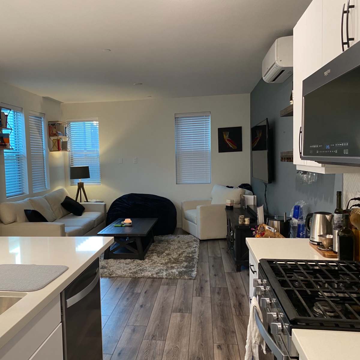 A modern kitchen and living area featuring white cabinetry, a gas stove, a seating area with a light sofa, and a dark coffee table.