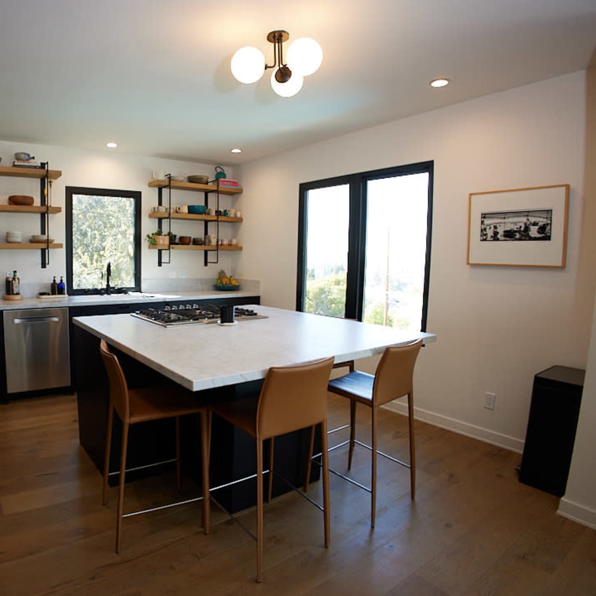 A modern kitchen featuring black cabinetry, a white countertop, and a central island with four wooden bar stools.