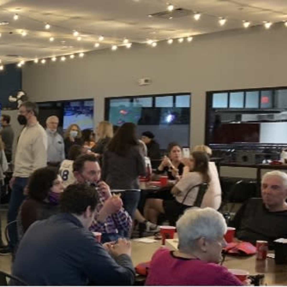 A lively indoor entertainment venue filled with people socializing, playing games, and watching sports on large screens.