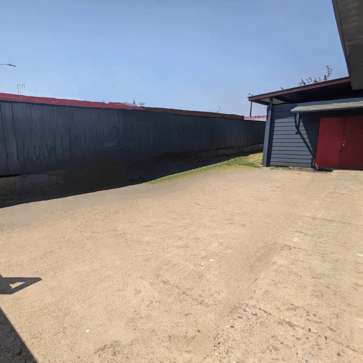 A gravel area next to a metal fence and a blue structure with a red door under a clear sky.