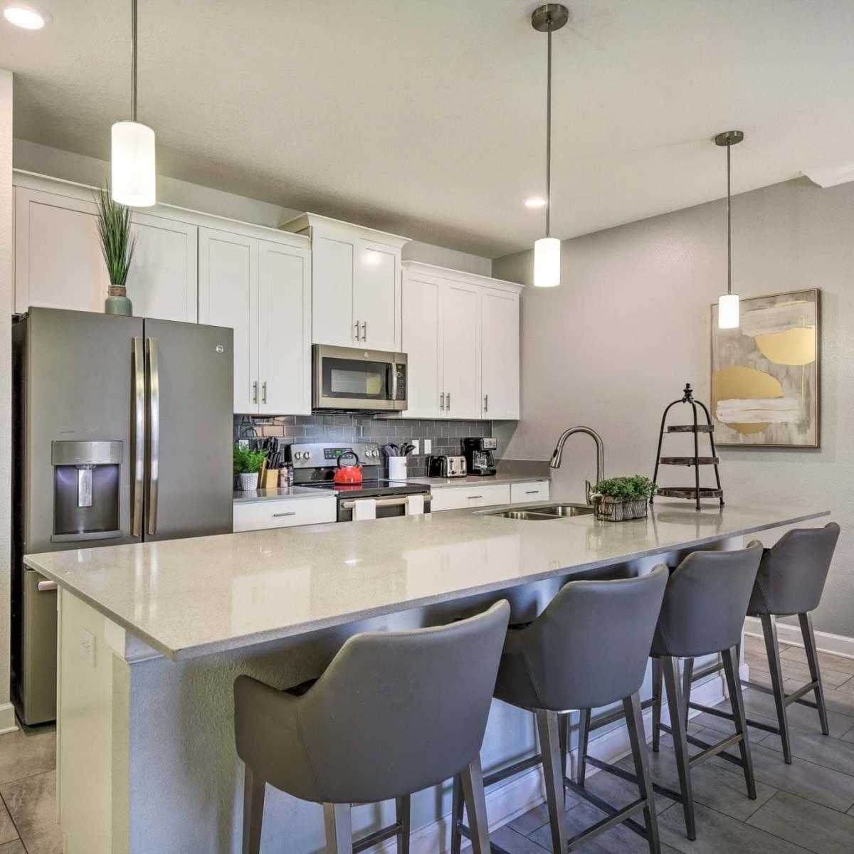 A modern kitchen with white cabinets, a large island with seating for four, and stainless steel appliances.