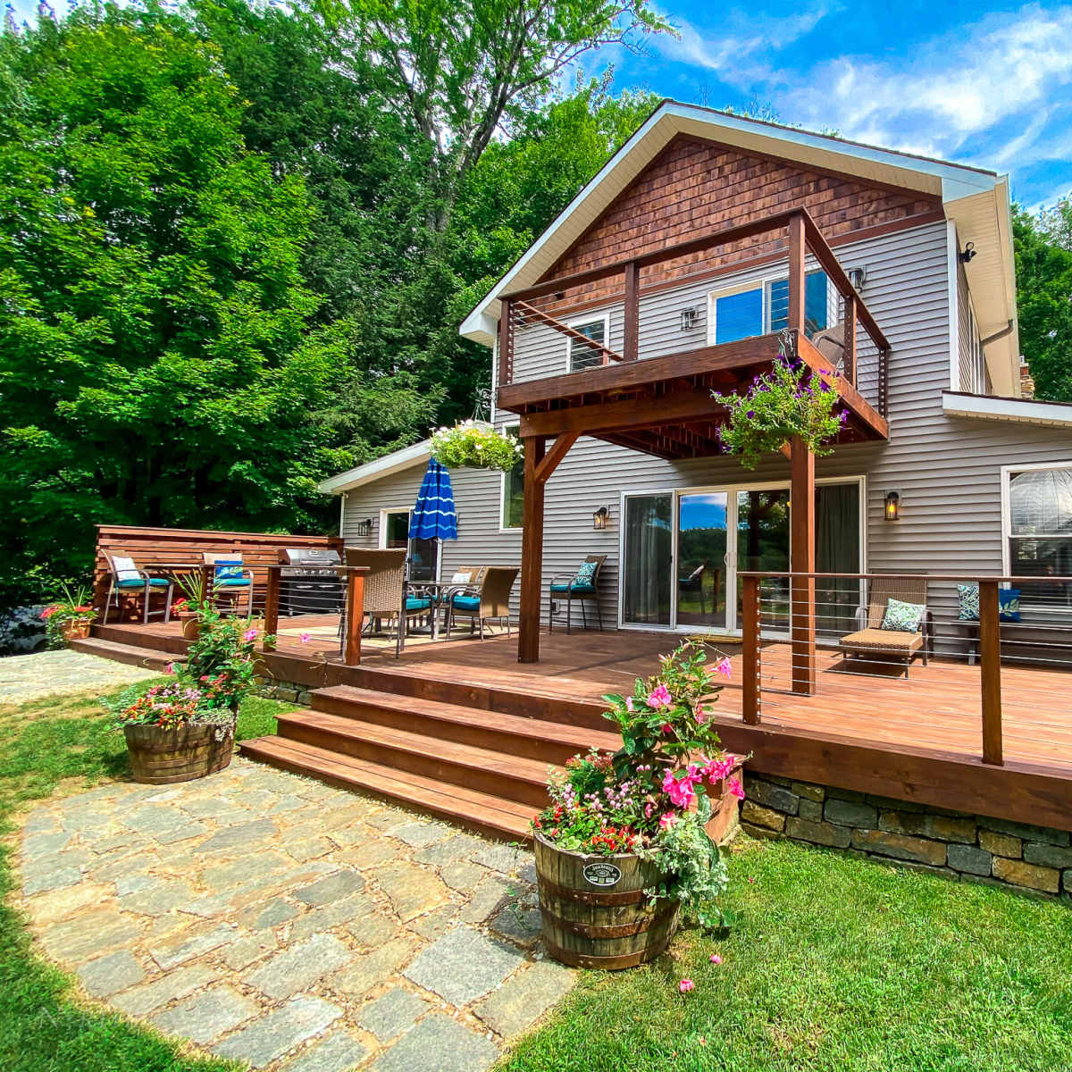 A two-story house with a wooden deck and a landscaped yard featuring stone pathways and flowerpots.