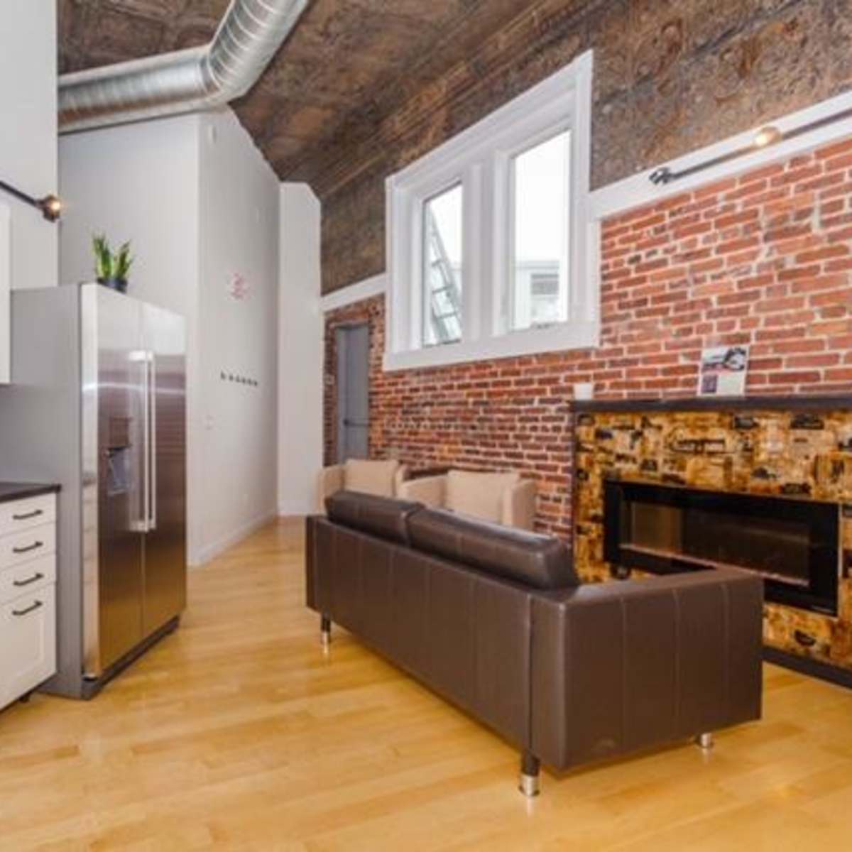 A modern kitchen and living area with exposed brick walls, stainless steel appliances, and hardwood flooring.