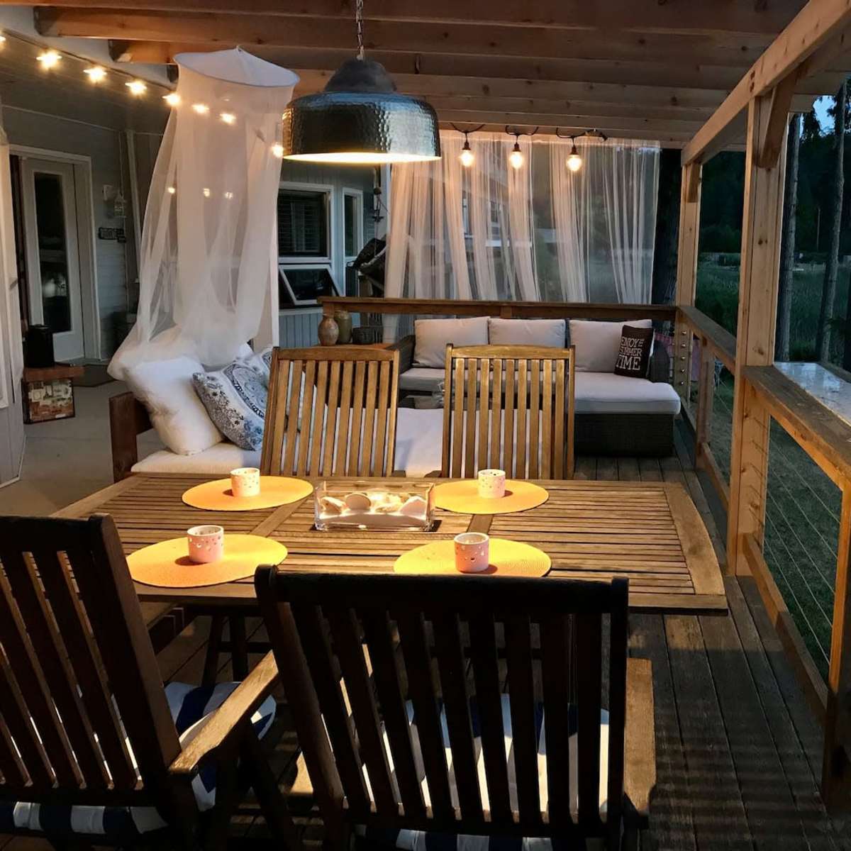 A wooden deck area with a table set for dining, surrounded by string lights and a cozy seating arrangement.
