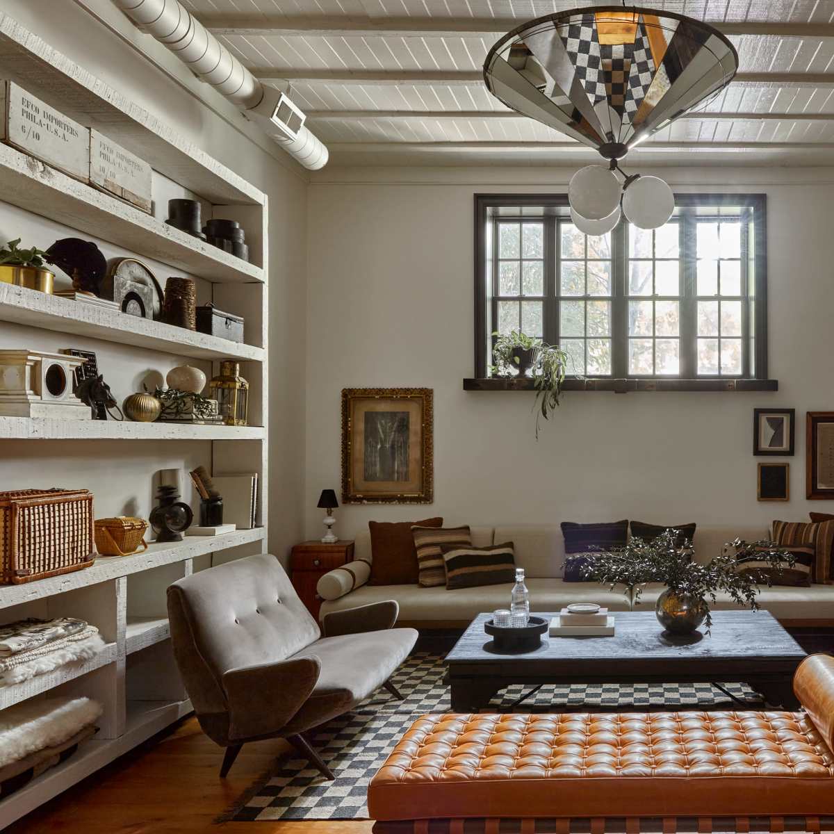 A stylish living room featuring a large window, a mix of seating options including a sofa and chairs, a central coffee table, and decorative shelves on the walls.