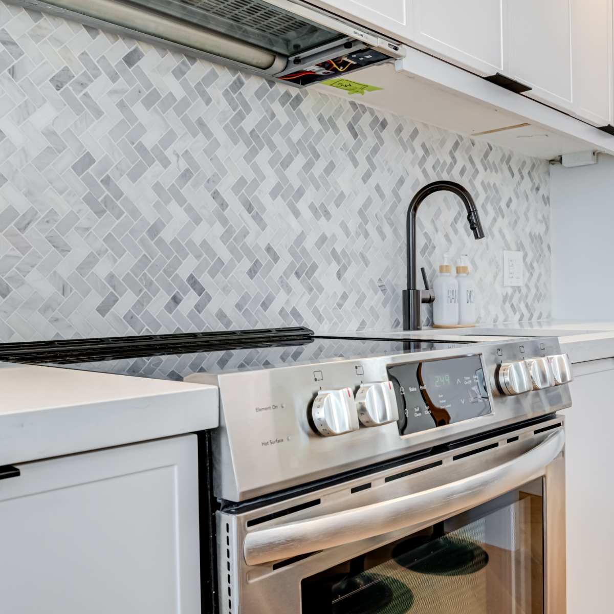 A modern kitchen with a stainless steel stove and a light grey herringbone-patterned backsplash.