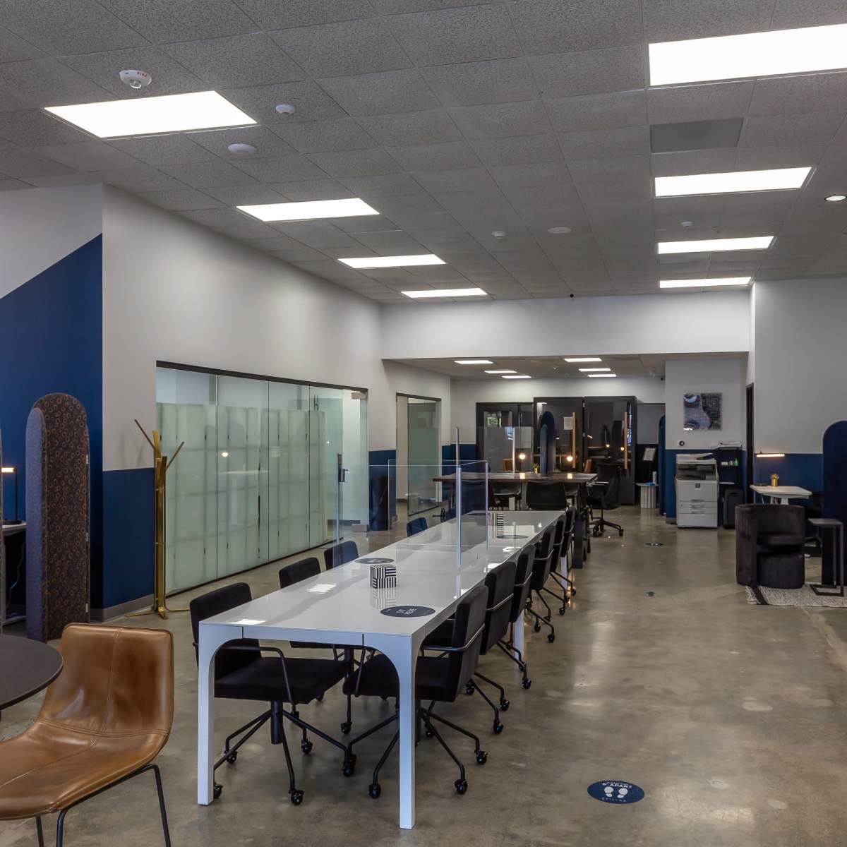 A modern office space with a long white table, dark chairs, and a glass wall separating different areas.