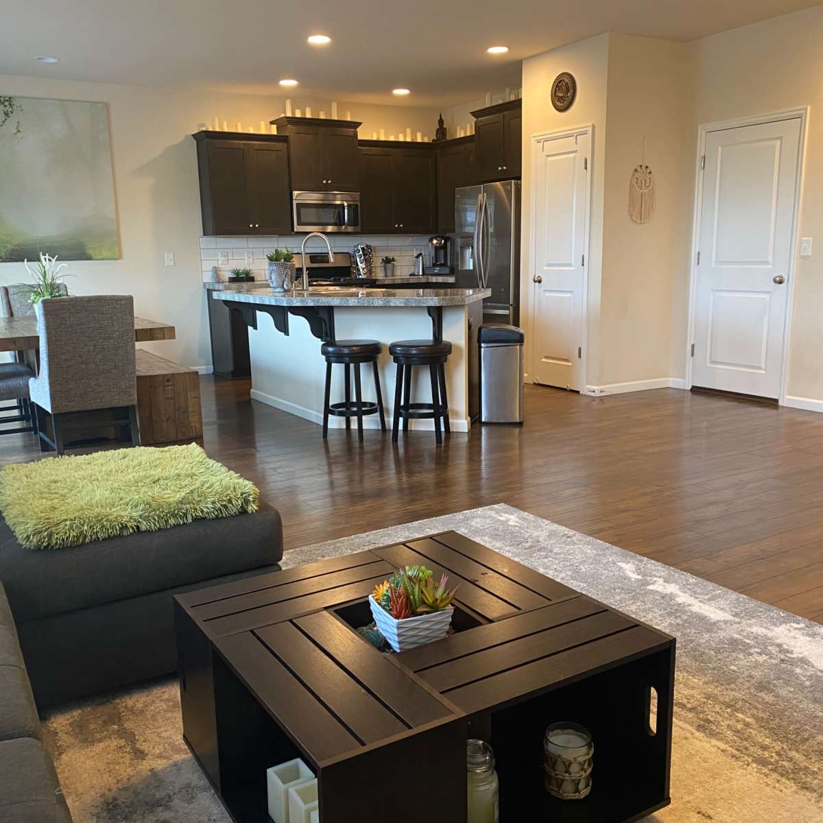 A modern living space with a gray sectional sofa, a coffee table, a dining area, and a kitchen in an open floor plan.