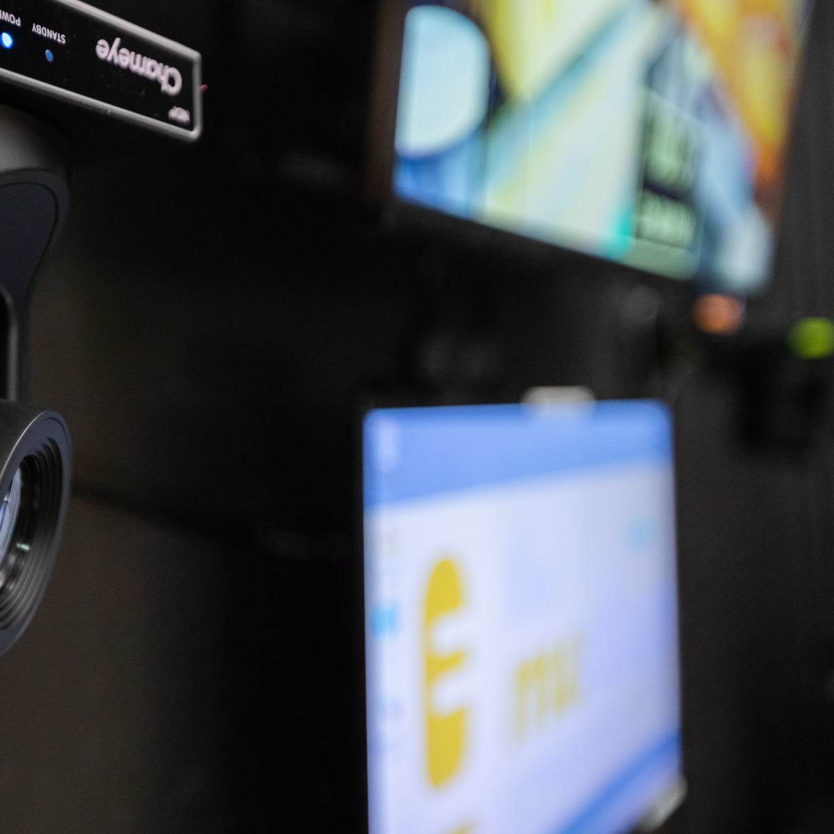A black camera is mounted on a wall beside multiple monitors displaying various graphics and information.