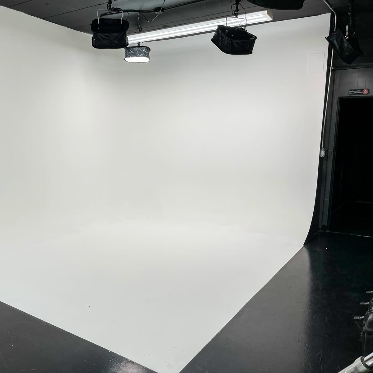 A photography studio with a seamless white backdrop and overhead lighting.