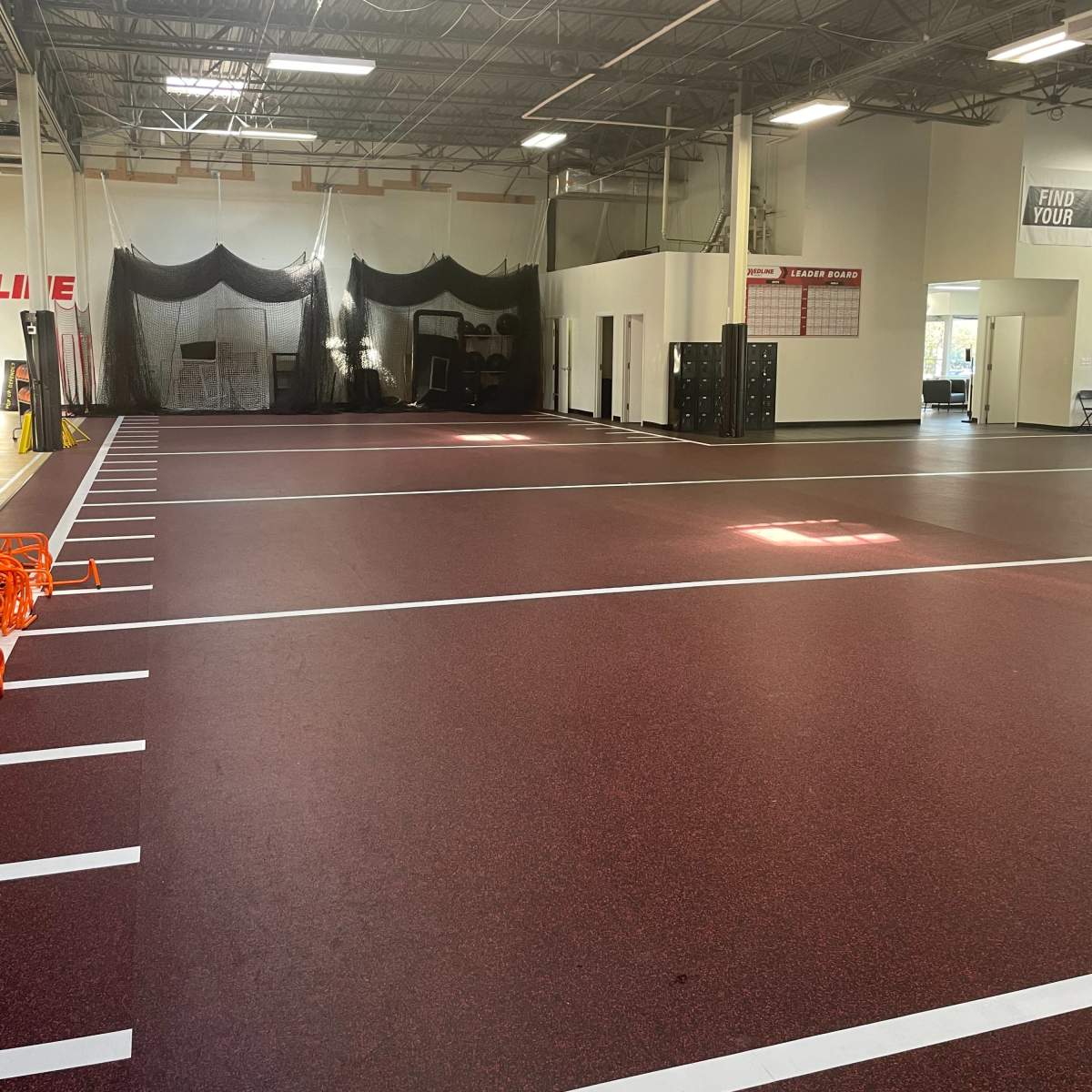 A large indoor training facility with red and white flooring, marked lanes, and various equipment in the background.