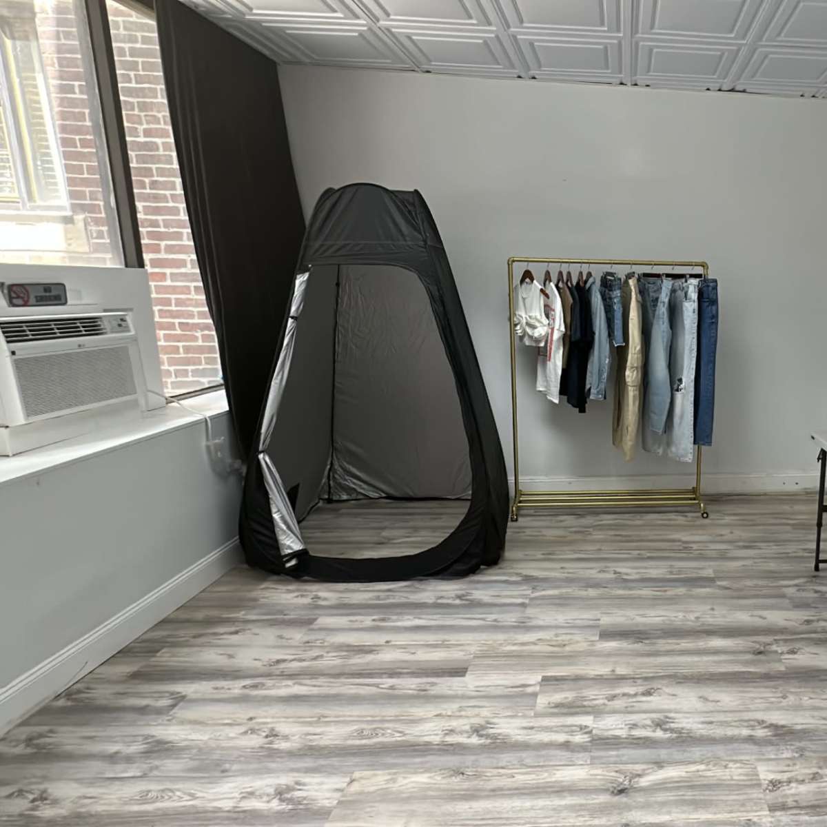 A sparsely furnished room with a changing tent, a rack of clothing, and a table with various items.