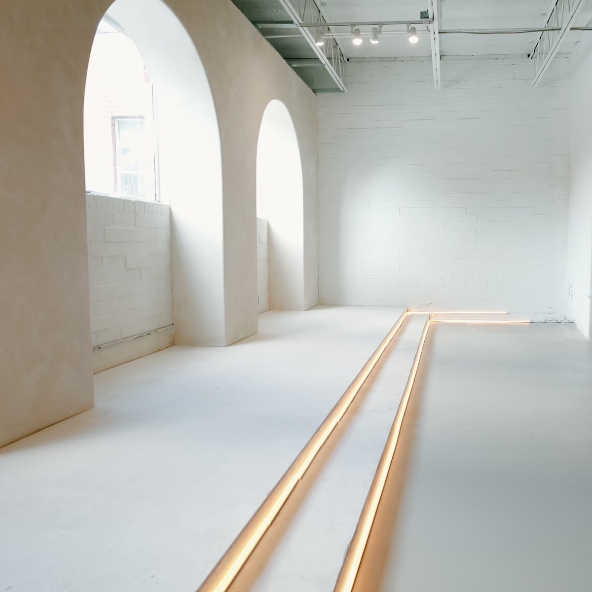 A minimalist room with arched windows, smooth white walls, and warm lighting along the floor.