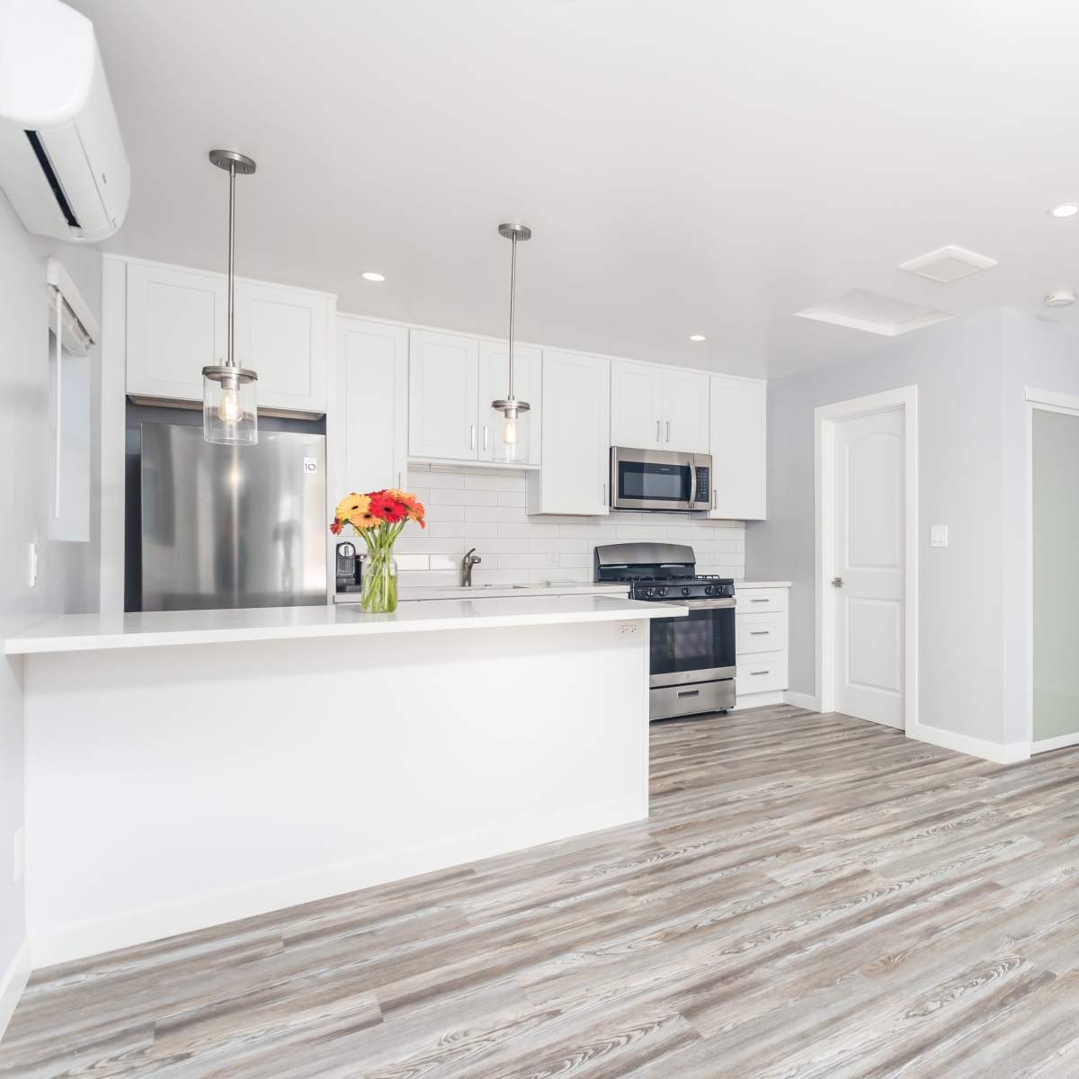 A modern kitchen and living area with white cabinetry, stainless steel appliances, and a light hardwood floor.