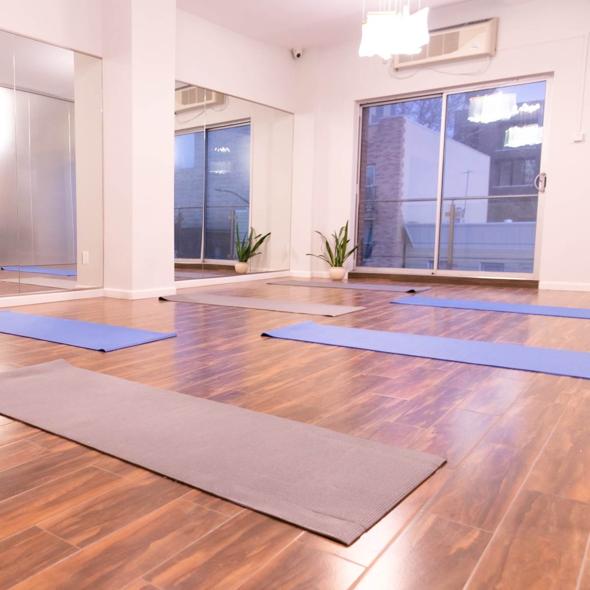 A spacious, well-lit yoga studio with several exercise mats arranged on a wooden floor.