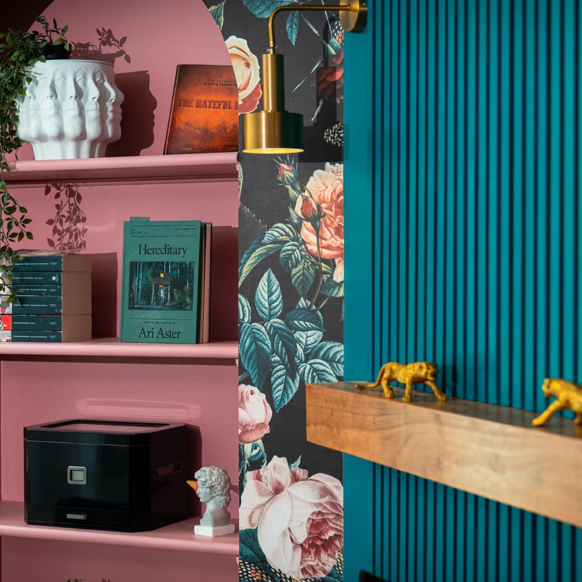 A colorful interior scene with a shelf displaying books, decorative objects, and a floral wallpaper backdrop.