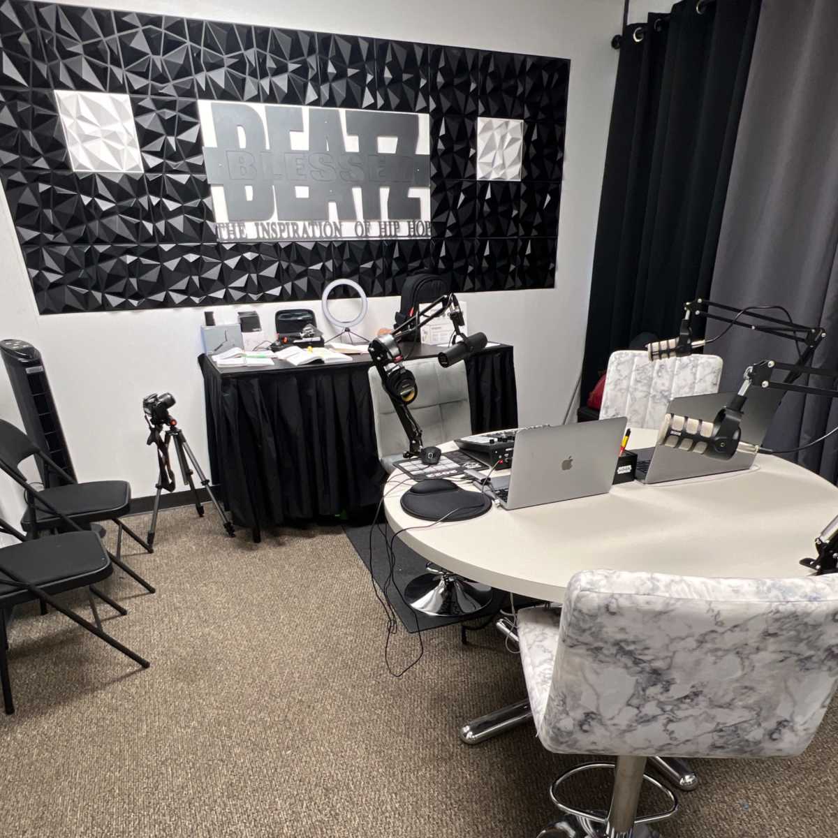 A recording studio setup with a round table, microphones, and equipment against a textured wall featuring the word "BEATZ."