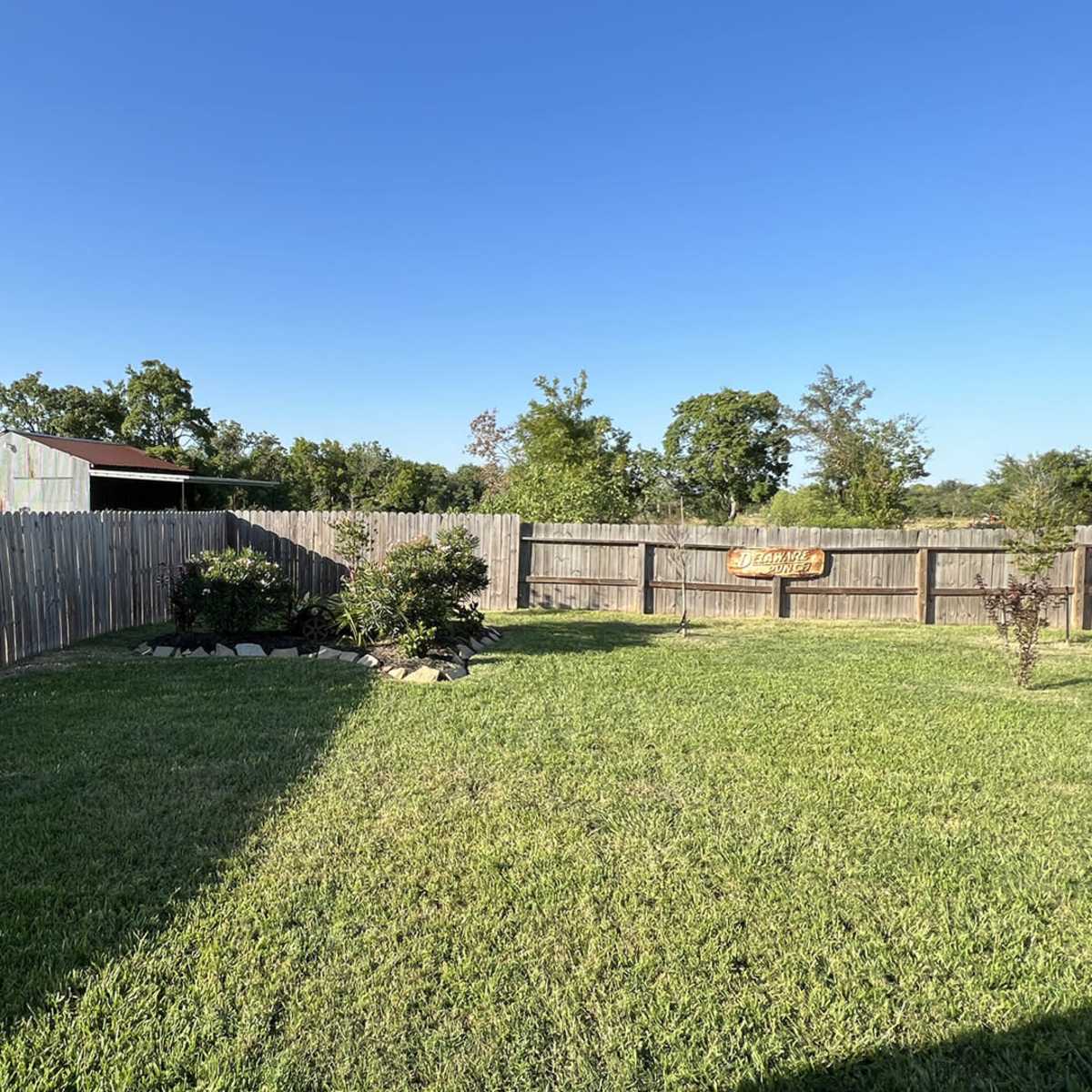 A well-maintained backyard with a wooden fence, green grass, and a shed in the background.