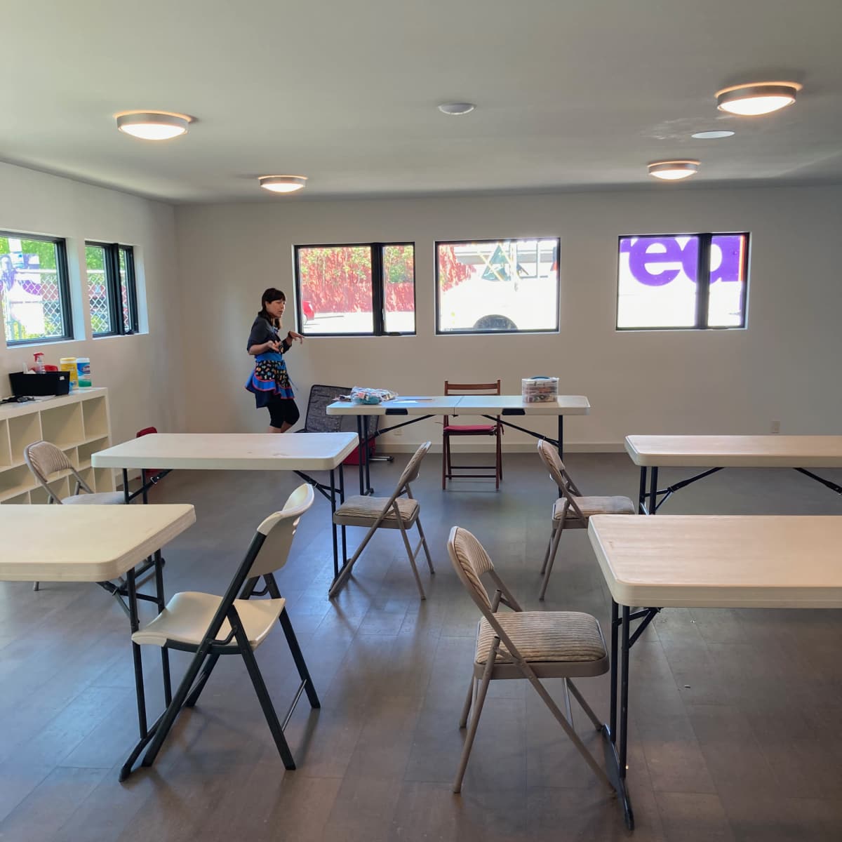 A person stands in a sparsely furnished room with several tables and chairs arranged in a neat configuration.