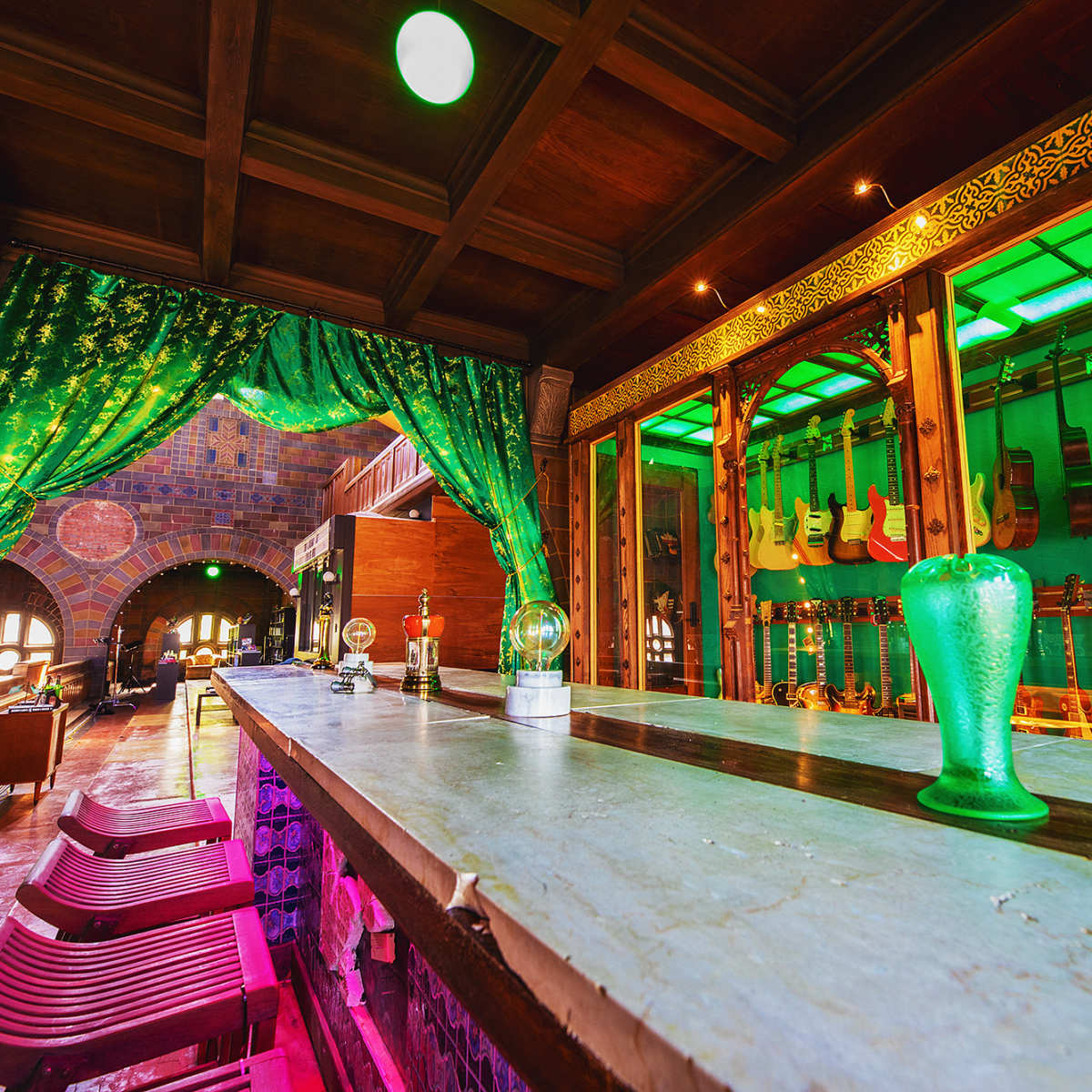 A dimly lit bar area with a green curtain, a stone counter, and a display of guitars in the background.