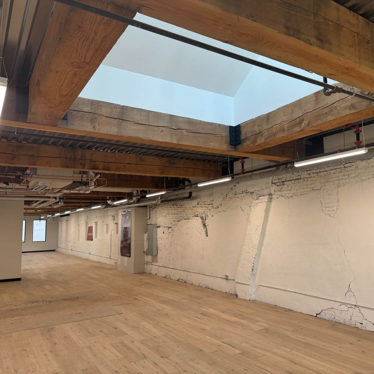An empty interior space featuring exposed wooden beams, a skylight, and cracked white walls.