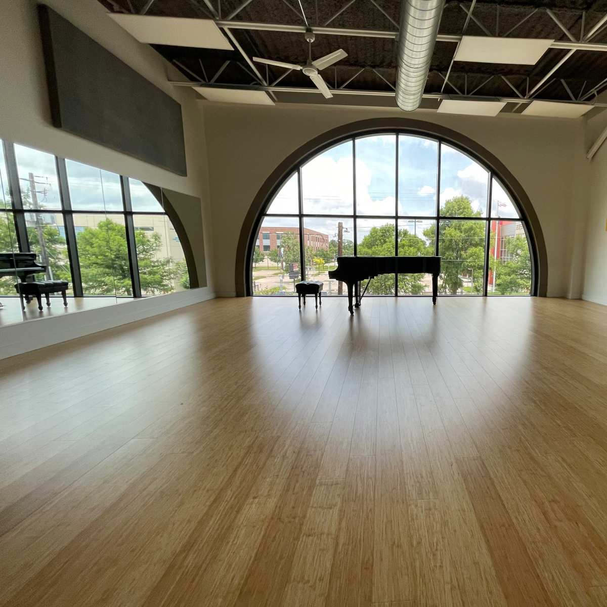 A spacious room with a large arched window, a grand piano, and wooden flooring.