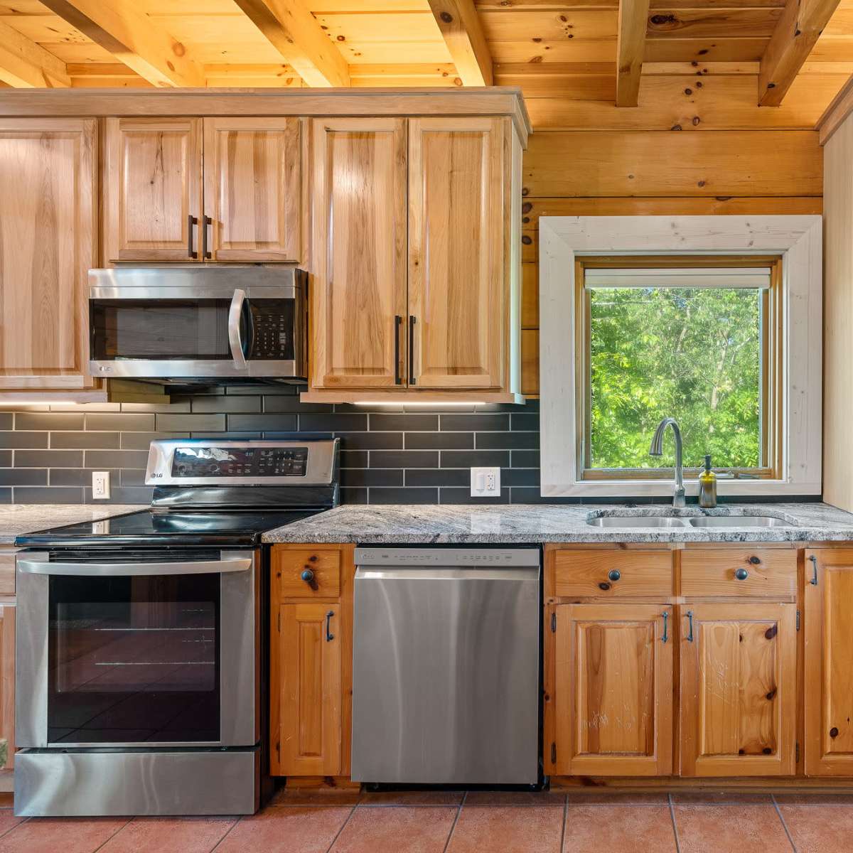 A modern kitchen features wooden cabinets, stainless steel appliances, and a window overlooking greenery.